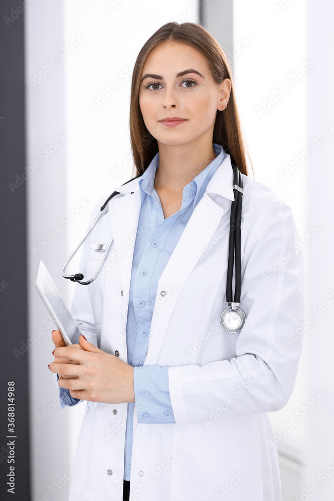 Doctor woman using tablet computer while standing straight near window in hospital. Happy physician at work. Medicine and health care concept Doctor woman using tablet computer while standing straight near window in hospital. Happy physician at work. Medicine and health care concept