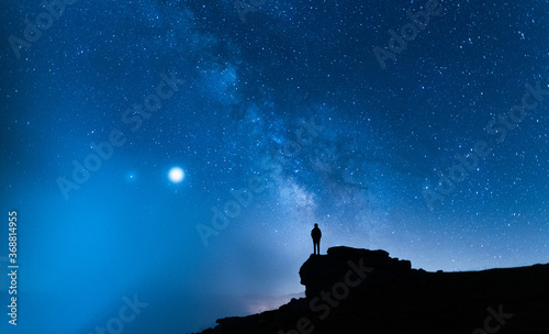 Person contemplating the vastness of the universe. Small silhouette of a man under the Milky Way and the magical starry sky. Concept of human smallness.