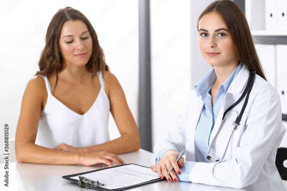 Doctor and happy patient talking while sitting at the desk. The physician or therapist discussing healthy lifestyle. Health care, medicine and patient service concept Doctor and happy patient talking while sitting at the desk. The physician or therapist discussing healthy lifestyle. Health care, medicine and patient service concept