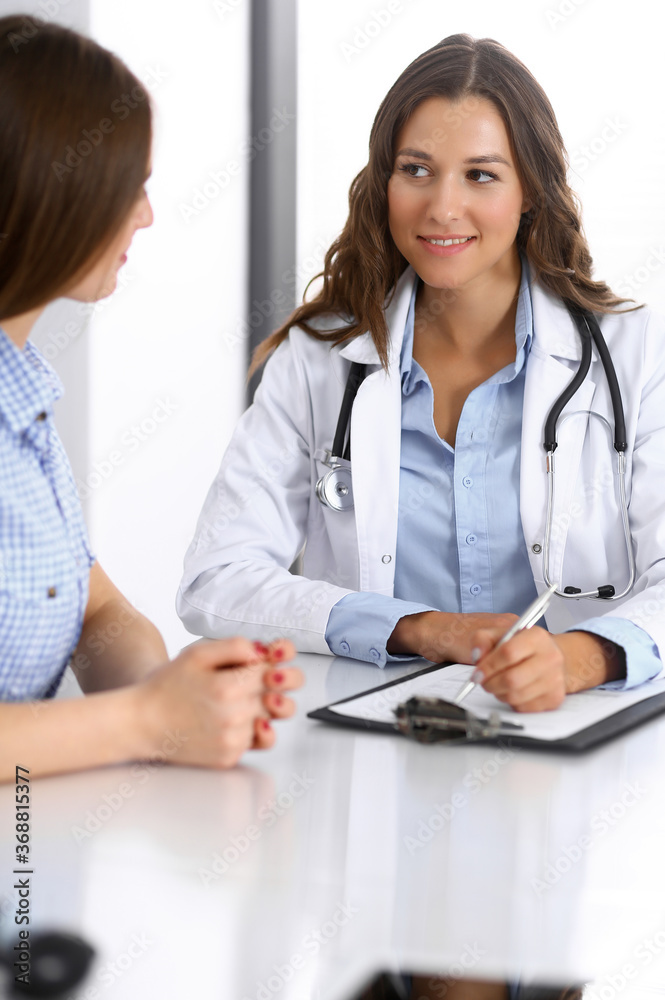 Doctor and happy patient talking while sitting at the desk. The physician or therapist discussing healthy lifestyle. Health care, medicine and patient service concept Doctor and happy patient talking while sitting at the desk. The physician or therapist discussing healthy lifestyle. Health care, medicine and patient service concept
