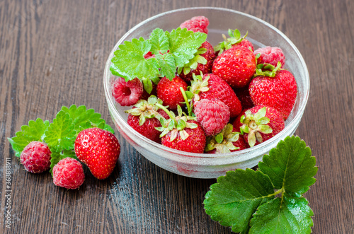 Raspberries with strawberries in a bowl on a brown wooden table with mint leaves