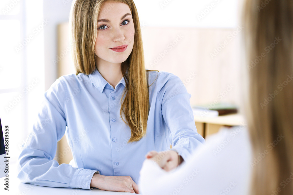 Business woman headshot while shaking hands with her female colleague or client in office. Casual white clothes style of business people. Audit, tax or lawyer concept Business woman headshot while shaking hands with her female colleague or client in office. Casual white clothes style of business people. Audit, tax or lawyer concept