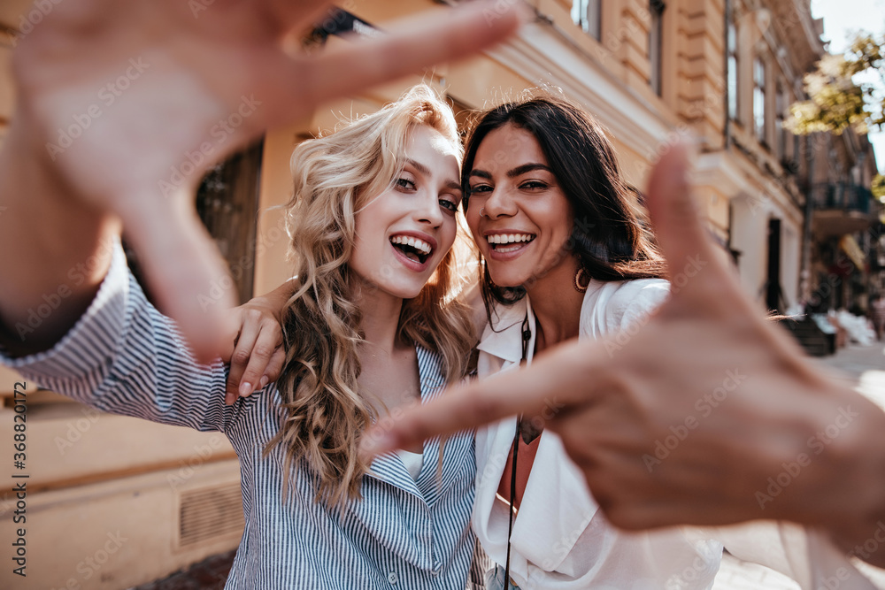 © Look! - Laughing blithesome woman with dark hair walking down the street with friend. Carefree blonde girl posing on city background. © Look! - Laughing blithesome woman with dark hair walking down the street with friend. Carefree blonde girl posing on city background.
