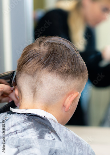 Vertical image Back view Close up caucasian pretty school boy trendy haircut at bright modern barbershop.