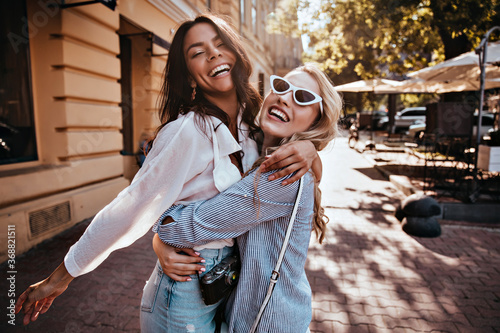 Glamorous woman in sunglasses embracing her sister. Outdoor photo of wonderful girls spending weekend together.
