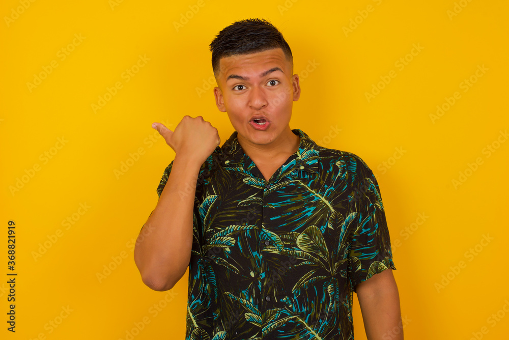 Horizontal shot of pretty young joyful shocked male points with thumb away, indicates something on blank wall isolated over gray background. Check this out. Ethnicity concept. Horizontal shot of pretty young joyful shocked male points with thumb away, indicates something on blank wall isolated over gray background. Check this out. Ethnicity concept.