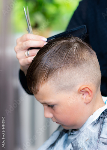 Close up caucasian pretty school boy combed after haircut at bright modern barbershop.