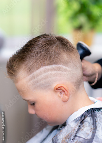 Side view caucasian american pretty school boy after haircut done stylish hairstyle wipes the hair at bright barbershop.