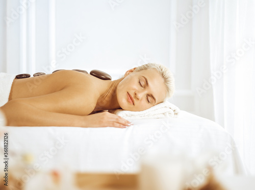 Beautiful blonde woman enjoying warm stones procedure with closed eyes. Spa concept