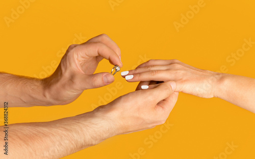 Young man putting engagement ring on his bride s finger over orange background  closeup