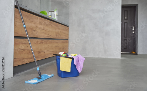 Cleaning equipment at home. Mop and plastic bucket with rags, detergents and different cleaning products on the floor in the modern kitchen