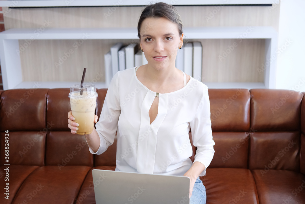 Smiling Caucasian woman happy with smell the aroma of latte iced coffee in modern cafe. She is relaxing in social online with on brow sofa. Lifestly and technology of women on holiday concept Smiling Caucasian woman happy with smell the aroma of latte iced coffee in modern cafe. She is relaxing in social online with on brow sofa. Lifestly and technology of women on holiday concept