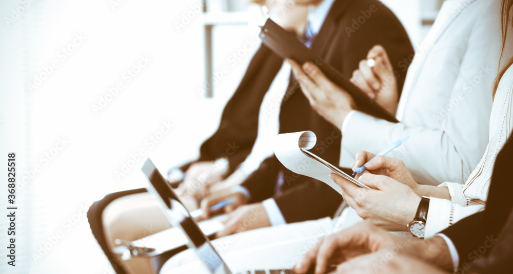 Business people working at meeting or conference, close-up of hands. Group of unknown businessmen and women in modern white office. Teamwork or coaching concept