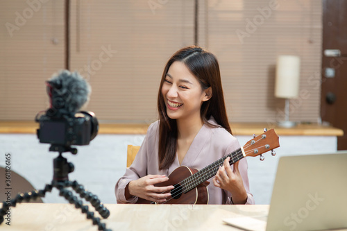 Asian teenage girl look at camera filming her self and playing ukulele guitar photo