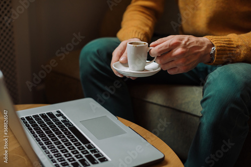 Cropped unrecognizable man drinking coffee in cafe, working.