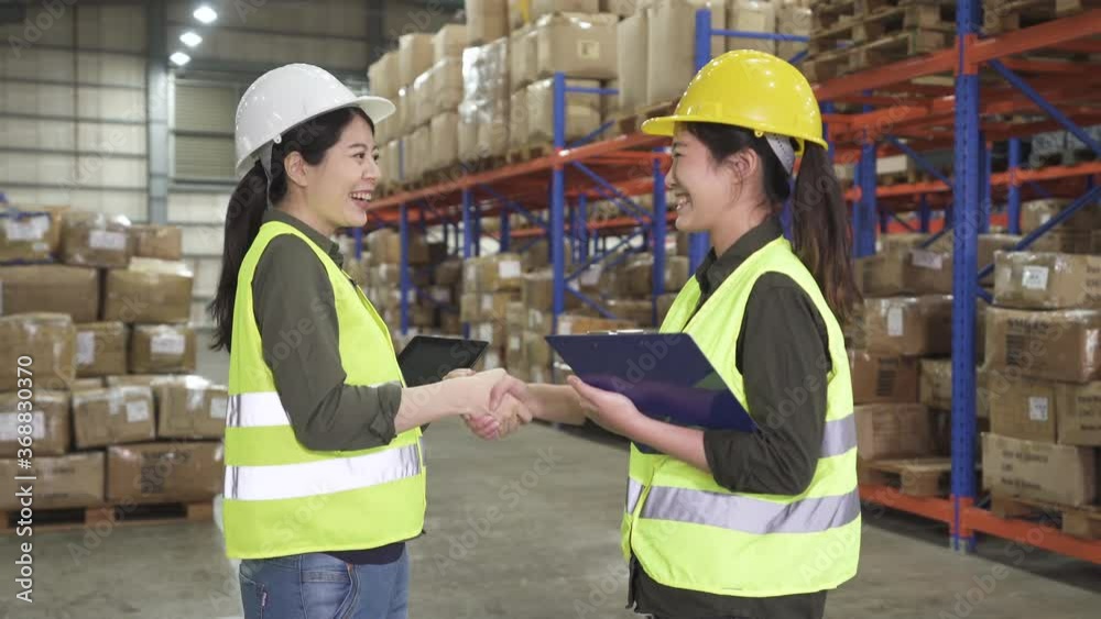 wholesale logistic people and export concept. two female manual workers with clipboard and tablet shaking hands and making deal at warehouse. asian women employees start up teamwork in stockroom. wholesale logistic people and export concept. two female manual workers with clipboard and tablet shaking hands and making deal at warehouse. asian women employees start up teamwork in stockroom.