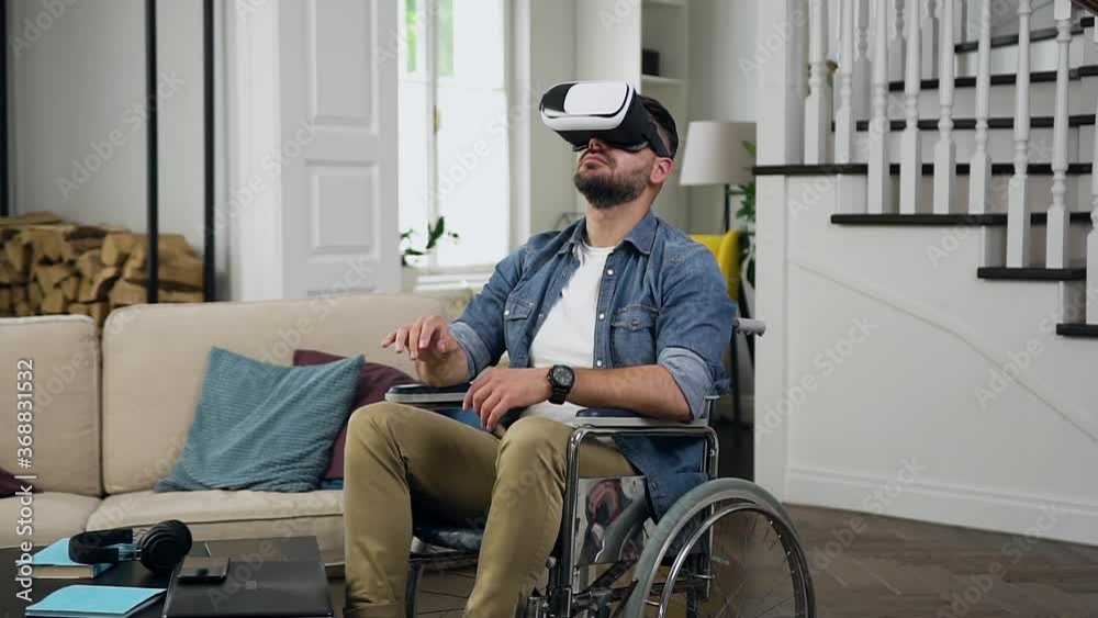 Portrait of good-looking attantive balanced 30-aged bearded man in wheelchair which working on imaginary screen using virtual reality headset Portrait of good-looking attantive balanced 30-aged bearded man in wheelchair which working on imaginary screen using virtual reality headset