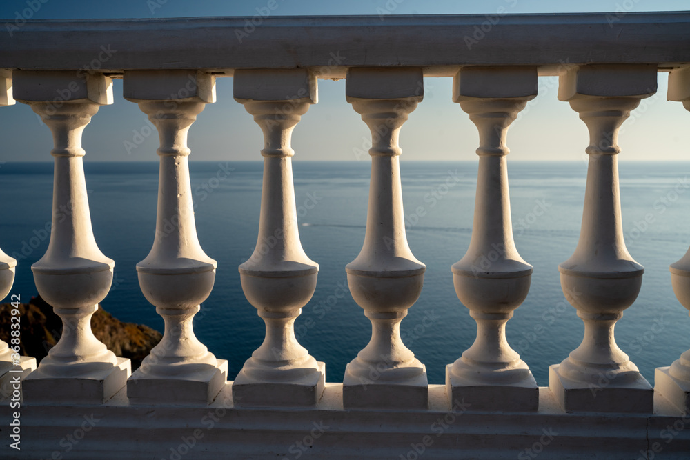 Fototapeta premium Classic balustrade on the embankment against the sea. White balcony over the sea. Promenade with a beautiful view of the sea on a clear day. Close-up of the balustrade by the sea