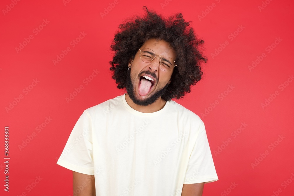 Handsome Caucasian man with happy and funny face smiling and showing tongue. Wearing casual clothes and standing against gray studio background. Handsome Caucasian man with happy and funny face smiling and showing tongue. Wearing casual clothes and standing against gray studio background.