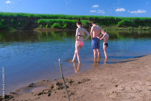 Barefooted family in swimsuits in river walking in water at Summer warm day. Mom, son and dad trying to bath in river, they are going to swim. Outdoors summer activity. Woman, man and child boy.