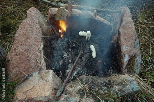 Sausages and bread on tree sticks above the campfire.