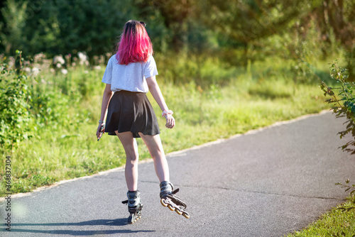 Sporting girl roller skating in a park on summer day.
