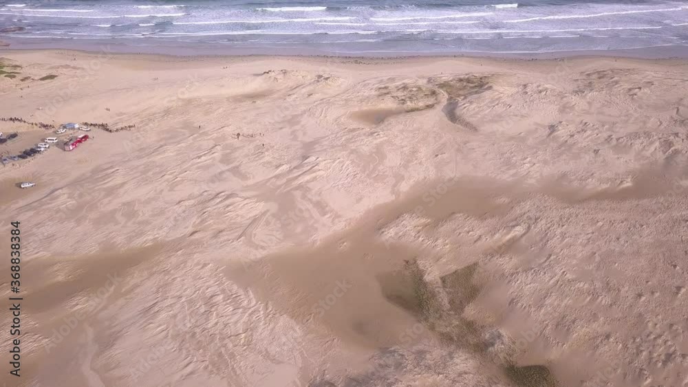 Aerial zoom in to a wide sandy beach with white waves and sand dunes at Stockton Beach. New South Wales, Australia. Aerial zoom in to a wide sandy beach with white waves and sand dunes at Stockton Beach. New South Wales, Australia.