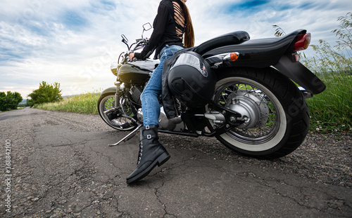Biker sits on a motorcycle standing on a countryside cracked asphalt road.