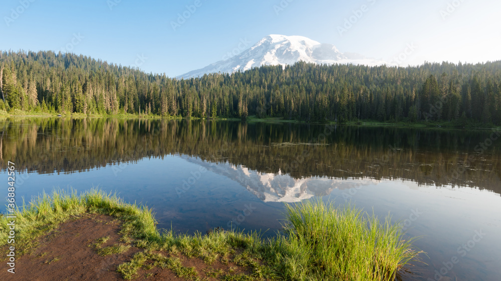 Mount Rainier, Washington mountain peak with a reflection in the water, surrounded by green trees.