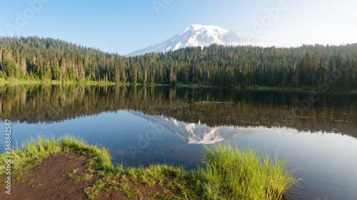 Mount Rainier, Washington mountain peak with a reflection in the water, surrounded by green trees.