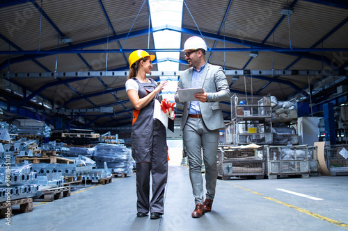 Manager supervisor and industrial worker in uniform walking in large metal factory hall and talking about increasing production. photo