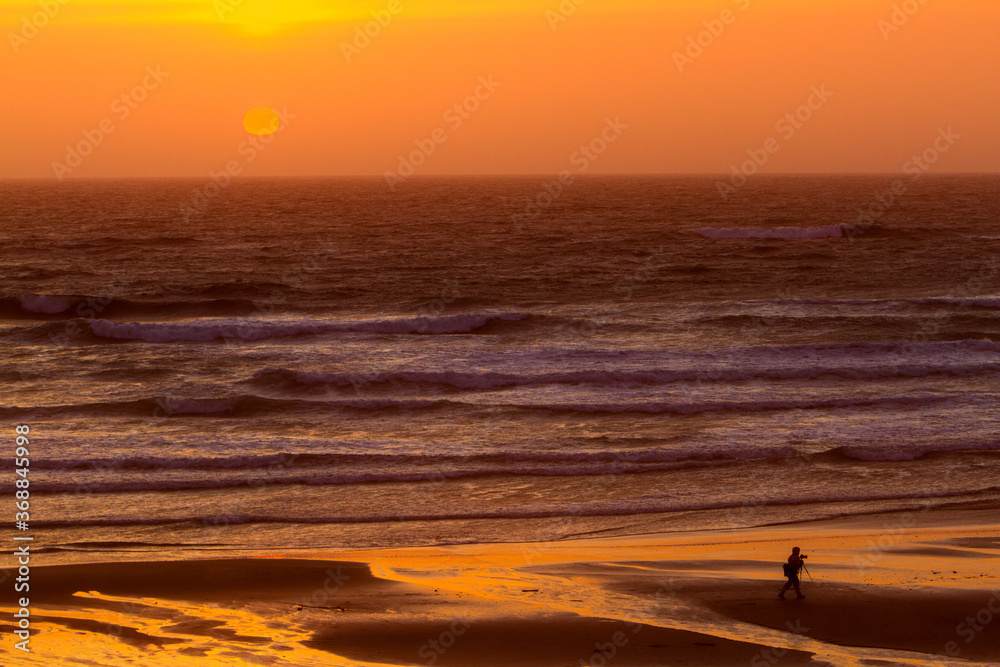 The sun setting over the pacific ocean with a silhouette of a photographer with his tripd at Seaside, Oregon