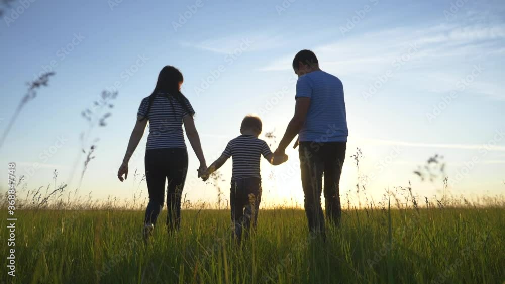 Happy family. Mom dad and son in an outdoor team walk through a green meadow at sunset. Healthy, active lifestyle of a married couple. Parents with a child have fun. Happy family. Mom dad and son in an outdoor team walk through a green meadow at sunset. Healthy, active lifestyle of a married couple. Parents with a child have fun.