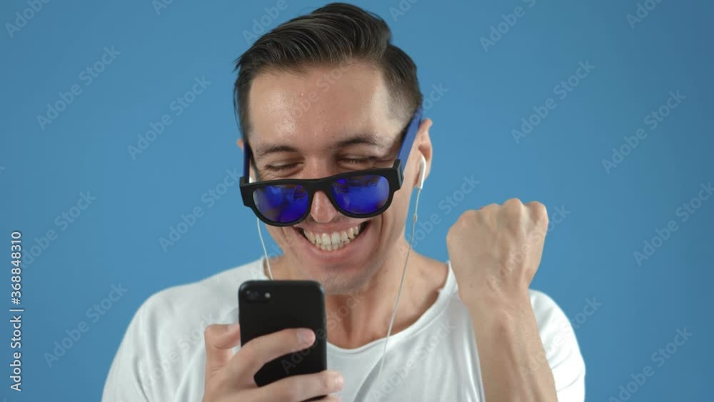 Surprised man winner hold smartphone read good news amazed by mobile online bet bid game win, happy male look at cell phone screen takes off sunglasses overjoyed by victory success Surprised man winner hold smartphone read good news amazed by mobile online bet bid game win, happy male look at cell phone screen takes off sunglasses overjoyed by victory success