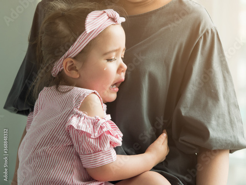 Photo Cute little Caucasian toddler girl crying with pain on mother's lap