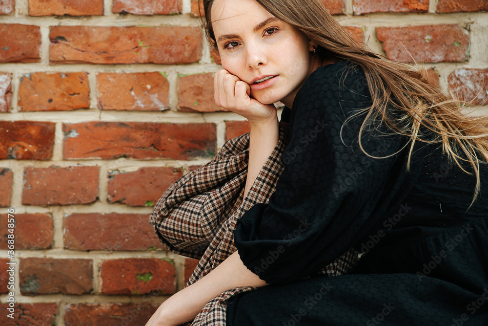 Sensual portrait of a young woman in a long black dress in front of a brick wall
