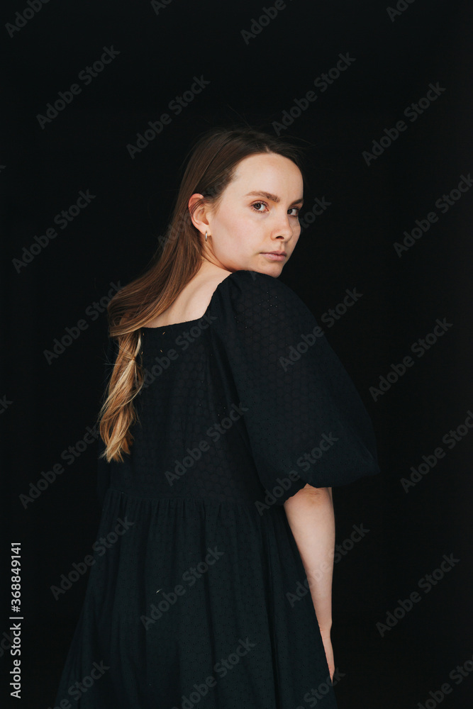 Woman looking at the camera over her shoulder. In black dress over black Woman looking at the camera over her shoulder. In black dress over black