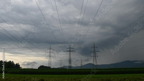 Time lapse of storm clouds moving over farmland grassland farming meadow field and high-voltage transmission electric power lines. Summer storm forming. Zoom in, low angle