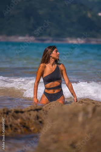 Lifestyle, Caucasian brunette in a luxurious black swimsuit with sparkles enjoying the summer at sea. Getting wet with the water of the waves