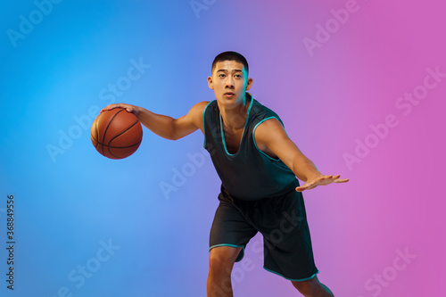 Winner. Young basketball player in action, motion on the run on gradient background in neon. Concept of sport, movement, energy and dynamic, healthy lifestyle. Training, practicing, trendy colors.