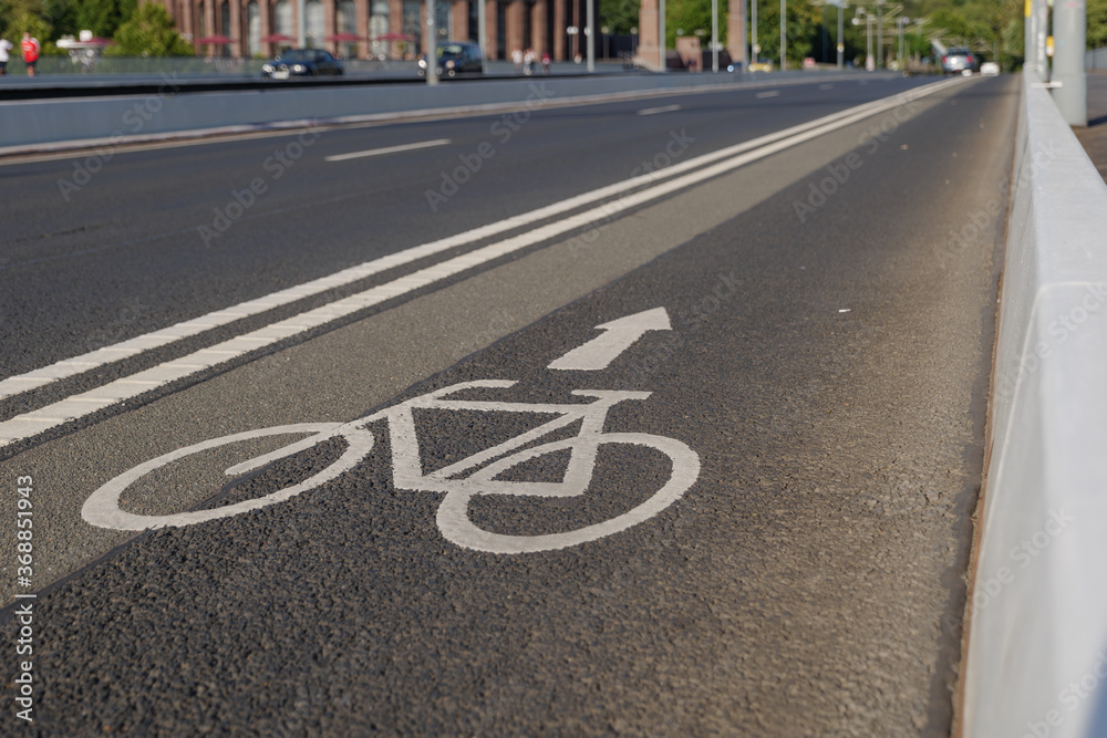 Obraz premium Selected focus view of white bicycle and arrow icon symbol on bicycle lane beside the road on the bridge cross Rhine River in Düsseldorf, Germany. Cycling friendly city concept in Europe. 