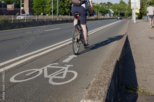 Selected focus view at white bicycle icon symbol and people ride bicycle on bicycle lane beside road on the bridge cross Rhine River in Düsseldorf, Germany. Cycling friendly city concept in Europe. 