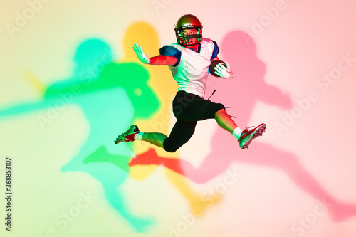 American football player isolated on gradient studio background in neon light with shadows. Professional sportsman during game playing in action and motion. Concept of sport, movement, achievements. © master1305