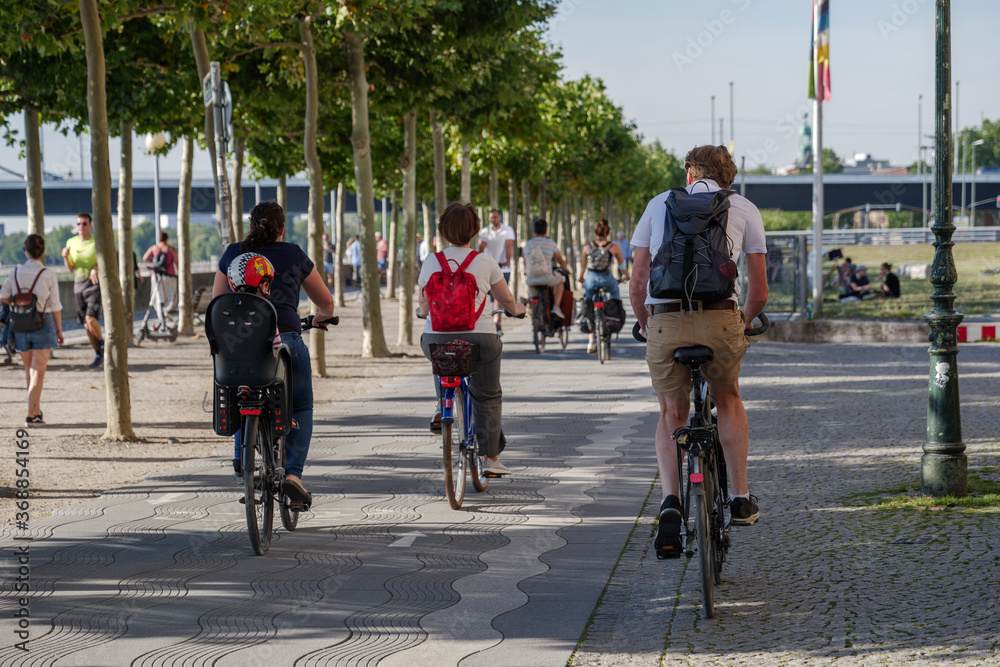 Group of cyclists ride bicycle on bicycle lane on promenade riverside of Rhein River in Düsseldorf, Germany. Cycling friendly city in europe. Eco friendly mobility transportation.