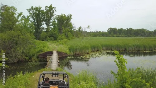 Wallpaper Mural 4k drone footage of unrecognizable man in a side by side UTV by a small river with lily pads and cloudy skies, trees, rural foot bridge by UTV camping trail in mid michigan orv trails Torontodigital.ca