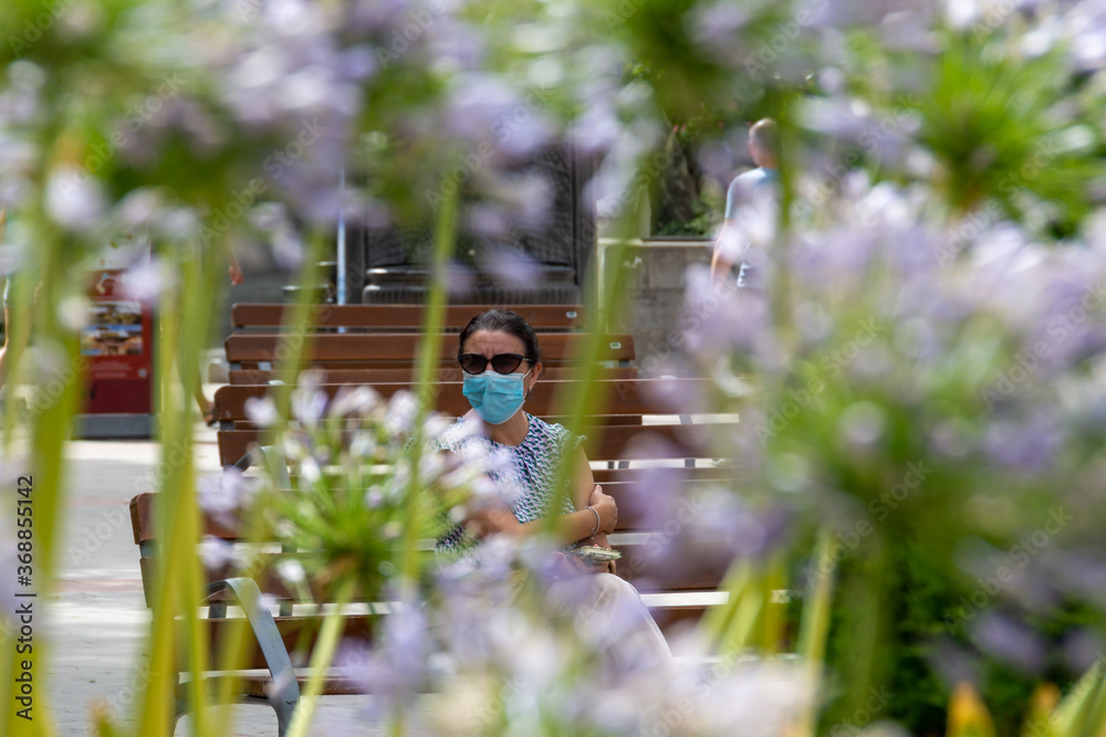 Woman with mask sitting in the park among flowers Woman with mask sitting in the park among flowers