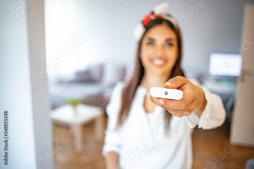 Young Woman Operating Air Conditioner With Remote Control. Portrait Of Smiling Young Woman Holding Remote Controller Of Air Conditioner At Home.