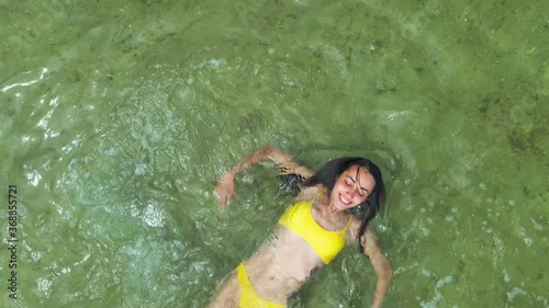 drone following relaxed beautiful laughing girl in yellow bikini swimming on back in calm sea