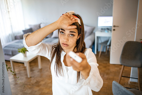 Woman feeling bad for summer heat haze. Close up view millennial woman at home exhausted by hot weather closed eyes feels unwell dying of heat holding in hand remote control 