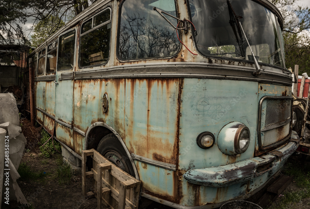 An abandoned bus standing in a forest parking lot among other abandoned vehicles